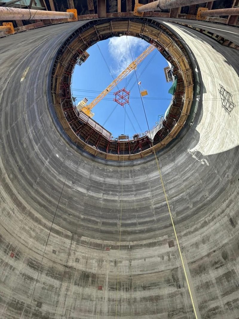 Interior de un silo de concreto visto desde la base, con el encofrado y la grúa torre recortados contra el cielo.